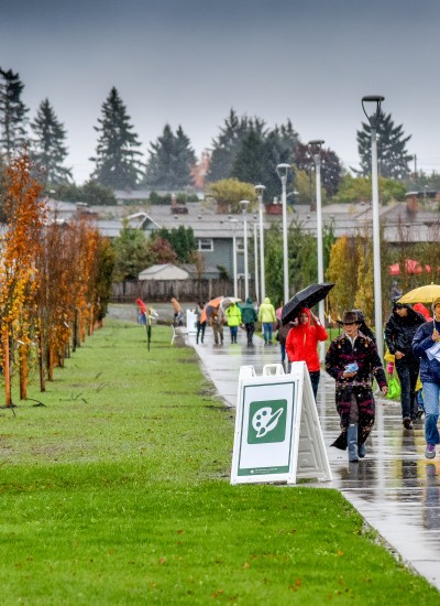 People walk down a park path on a rainy day. Homes and trees are in the distance behind them.