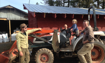 A child plays on a tractor while three adults stand nearby. One smiles at the camera.