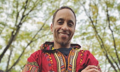 Eddie, standing outside, wears a colorful shirt and smiles at the camera