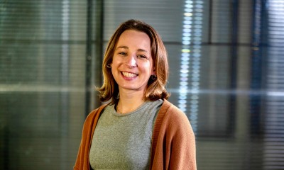 Anna stands against a glass wall and smiles